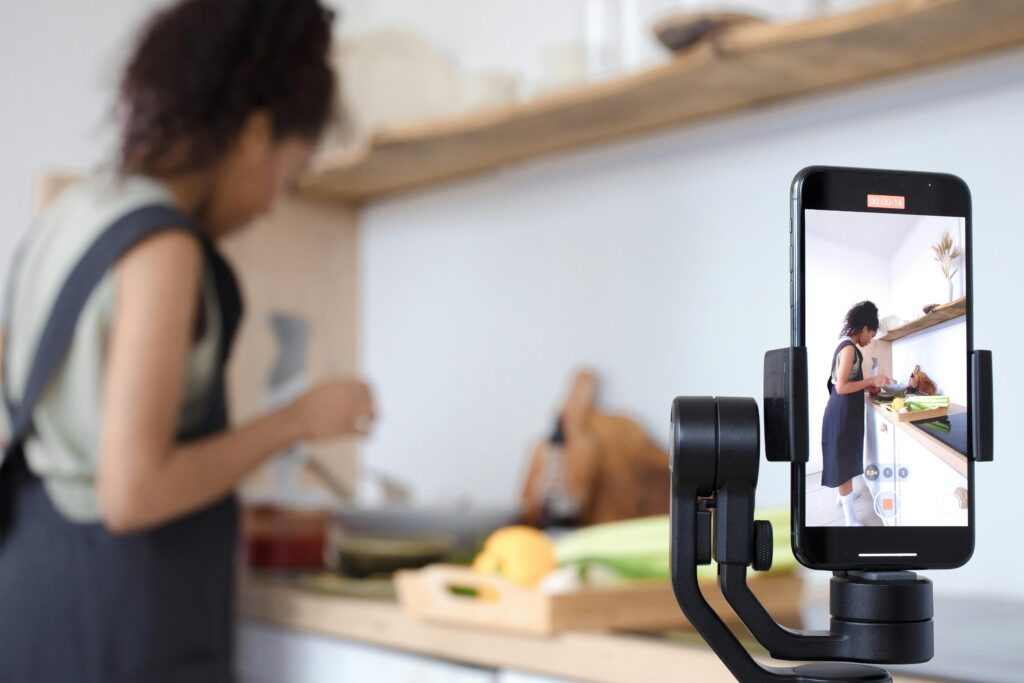 Woman using smartphone to record a cooking tutorial in a modern kitchen setting.